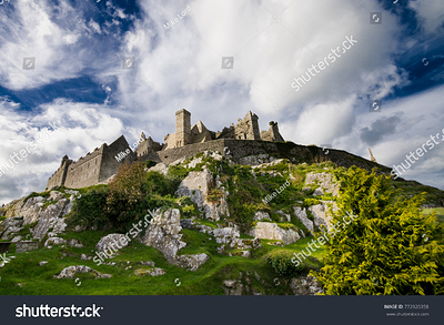 stock-photo-looking-up-at-medieval-castle-ruins-perched-atop-rock-outcrop-with-big-blue-sky-and-puffy-white-772920358
